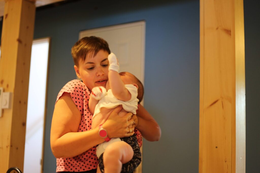 A parent in a polka-dot top holding a newborn upright against her chest, the baby's arm raised.
